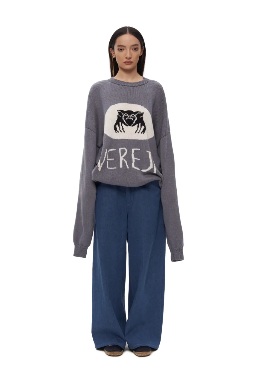 Графичный вязаный свитер с фирменным символом Vereja — Чихпауком. Модель выполнена в спокойном сером оттенке, который подчёркивает контрастный жаккардный рисунок: паук в овальном медальоне на груди и наивная надпись VEREJA ниже, будто выведенная от руки. Образ балансирует между детской непосредственностью, фольклором и арт-эстетикой бренда.
Свободный силуэт, спущенная линия плеча и плотная вязка создают ощущение уюта и защищённости — как у «бабушкиного» свитера, но в современной интерпретации. Подходит для многослойных образов и легко становится акцентной вещью в повседневном гардеробе.