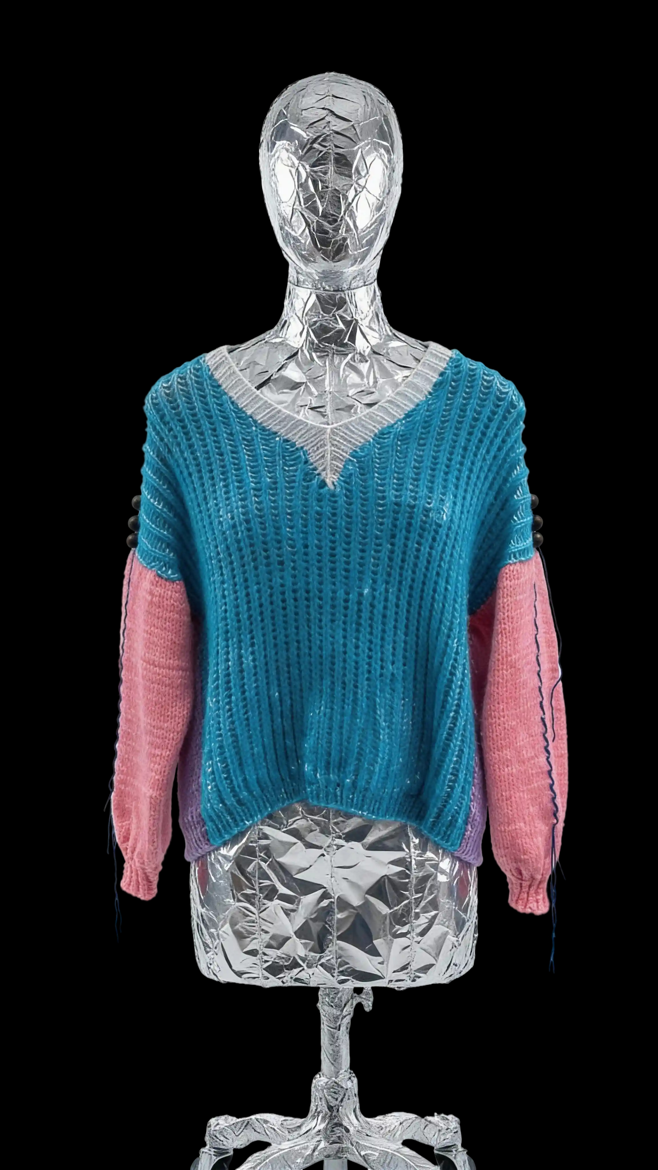 Голубой перед, фиолетовый зад, розовые рукава, синие вставки по бокам и холодная белая обтачка V-образного выреза — аккуратный колор-блок, который выглядит ярко, но не как маркерный набор.
По плечам идут ряды деревянных бусин — будто кто-то закрепил ими весь этот цвет, чтобы он никуда не разъехался. По швам рукавов — декоративная стёжка, добавляющая ещё немного движения и характера.