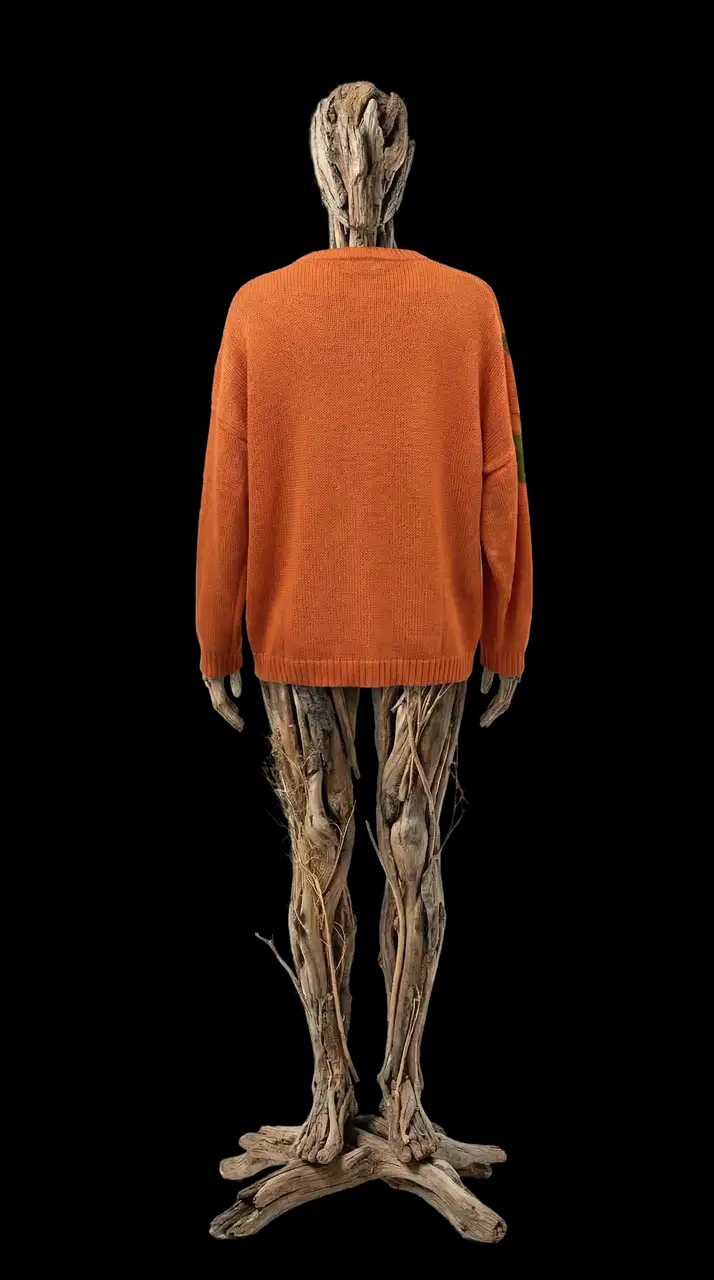Свитер с крупным графическим изображением перевёрнутого Чихпаука, связан из пряжи на основе крапивы — редкого, прочного и экологичного материала. Крапива даёт характерную сухую фактуру, плотность и ощущение «живой» вещи, которая со временем красиво меняется и адаптируется к телу.
Перевёрнутый Чихпаук — символ перехода, внутреннего напряжения и трансформации. Он выглядит одновременно наивно и тревожно, как рисунок из детской памяти или знак из личного мифа. Контрастное сочетание терракотово-оранжевого и приглушённого зелёного подчёркивает графику мотива и делает образ сильным, но не агрессивным.
Свободный унисекс-силуэт, спущенная линия плеча и мягкая посадка